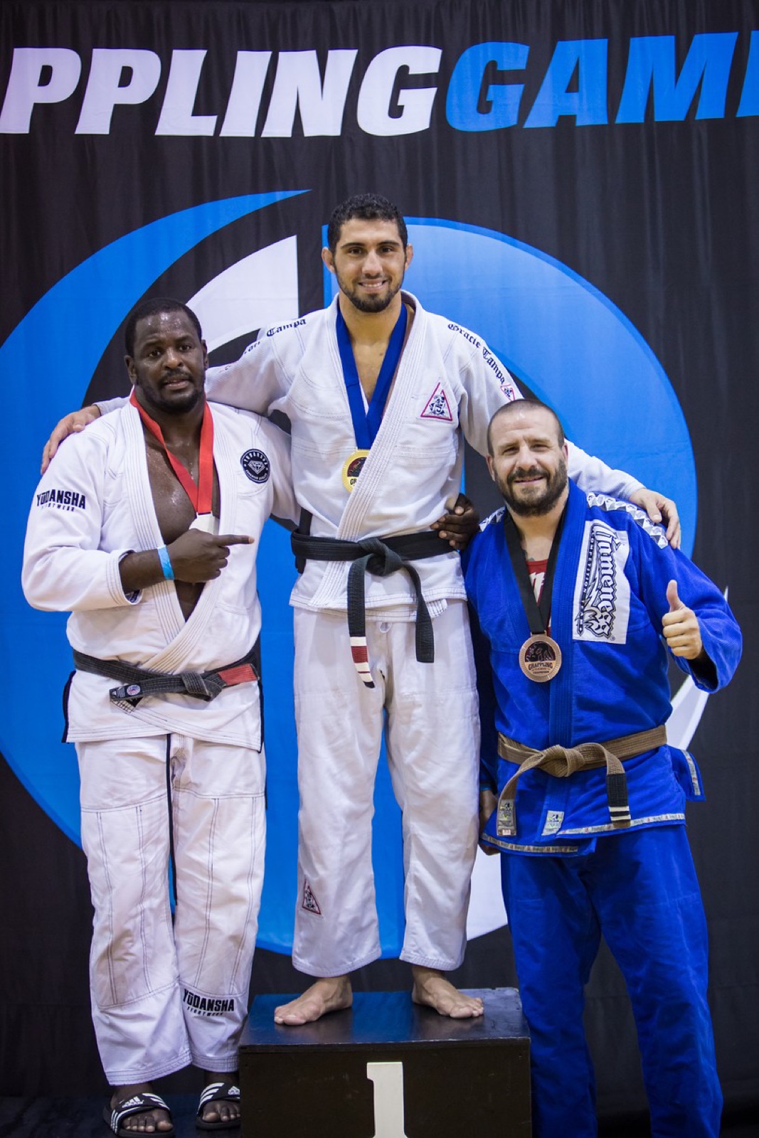 Sonny Parlin on the podium with a bronze medal at the Grappling Games, giving a thumbs up in a blue gi