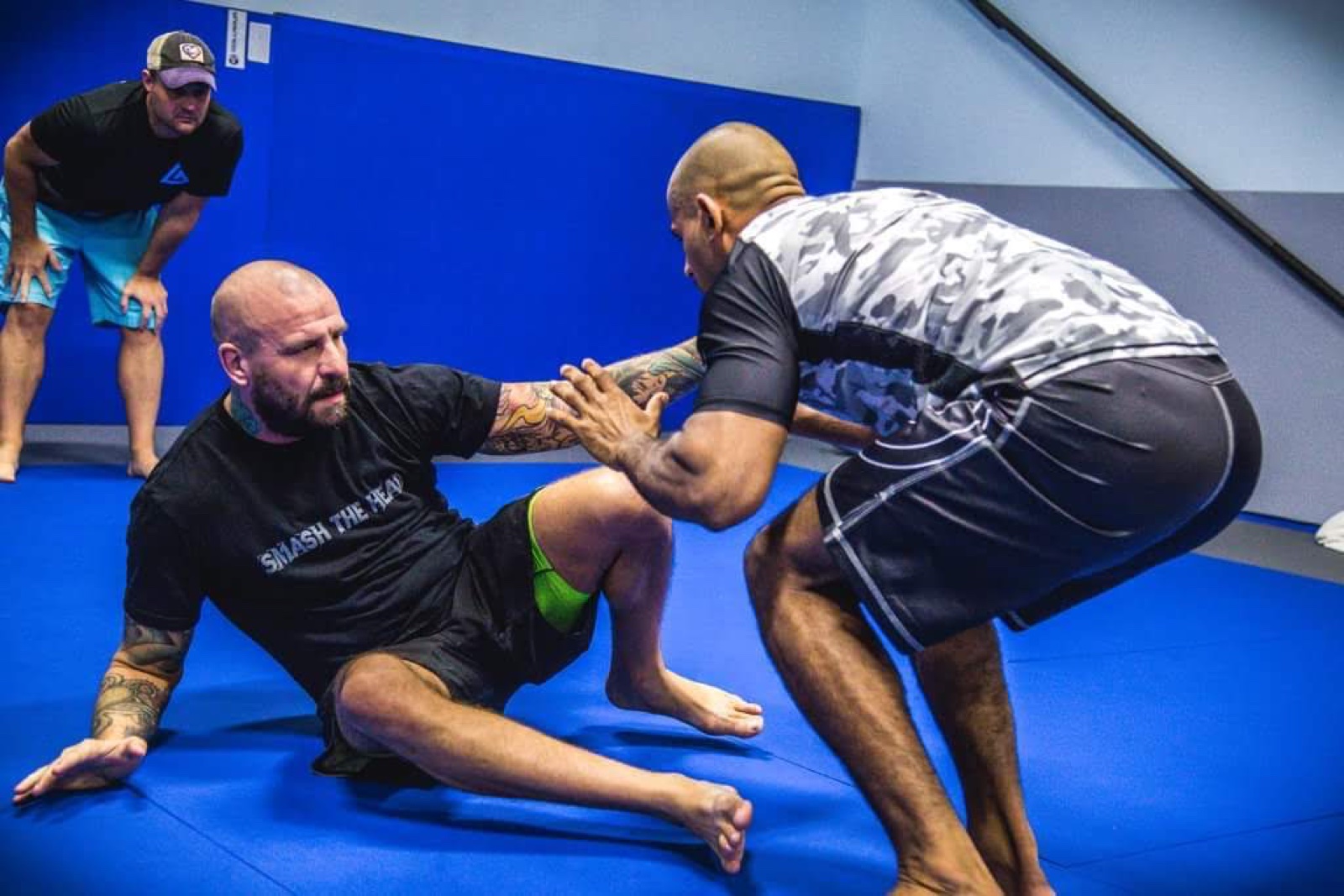 Sonny Parlin playing seated guard against a standing training partner on blue mats