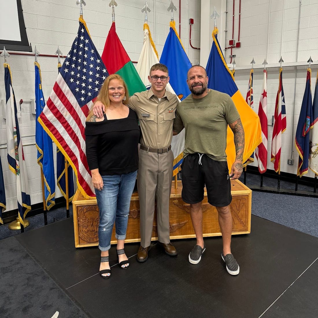 Sonny Parlin with his wife Kara and their son Jake in uniform, standing in front of a row of flags