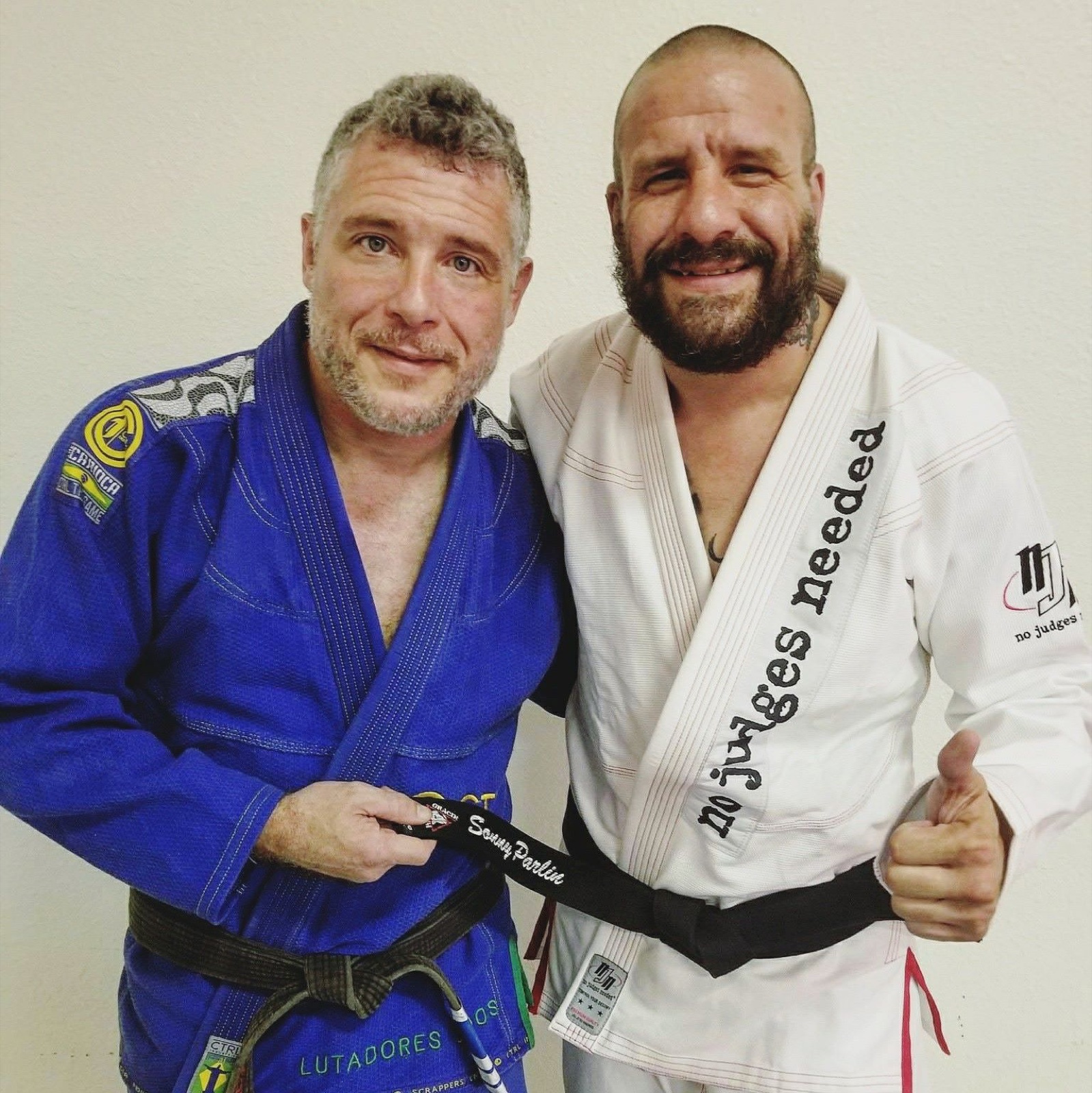 Rob Kahn in a blue gi handing Sonny Parlin his black belt