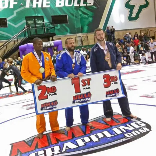 Sonny Parlin standing in first place on the podium at an MMAC Grappling tournament in a blue gi